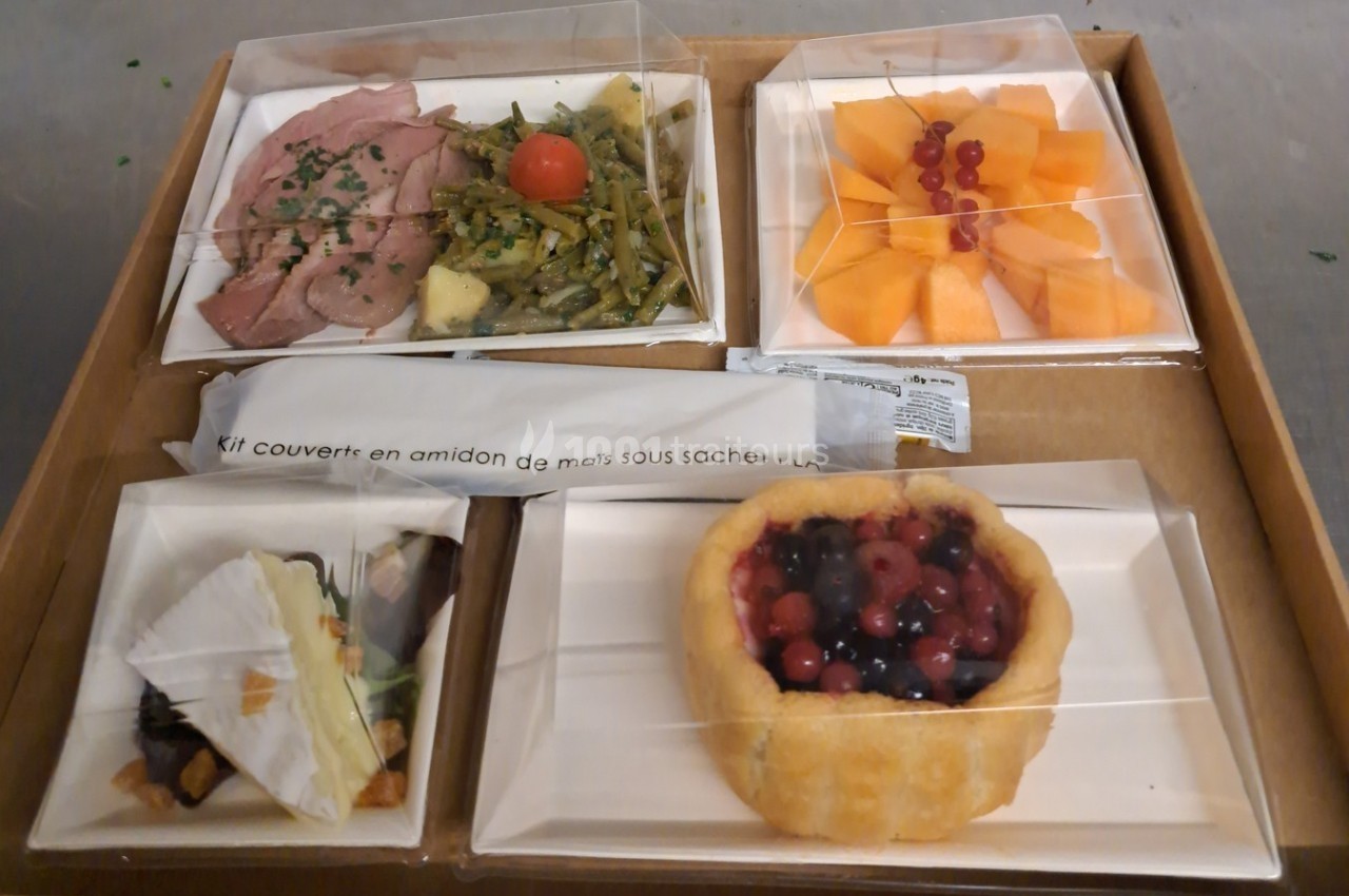 Plateau-repas avec viande, légumes, melon, dessert aux fruits rouges et pâtisserie, accompagné de couverts emballés.