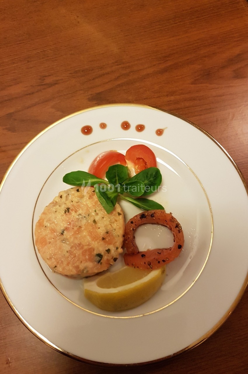 Assiette avec un tartare de saumon, rondelle de poivron grillé, citron, tomates, mâche et sauce décorative.