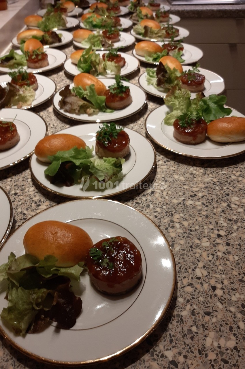 Assiettes dressées avec des mini-burgers, salade verte et sauce, alignées sur un plan de travail en pierre.