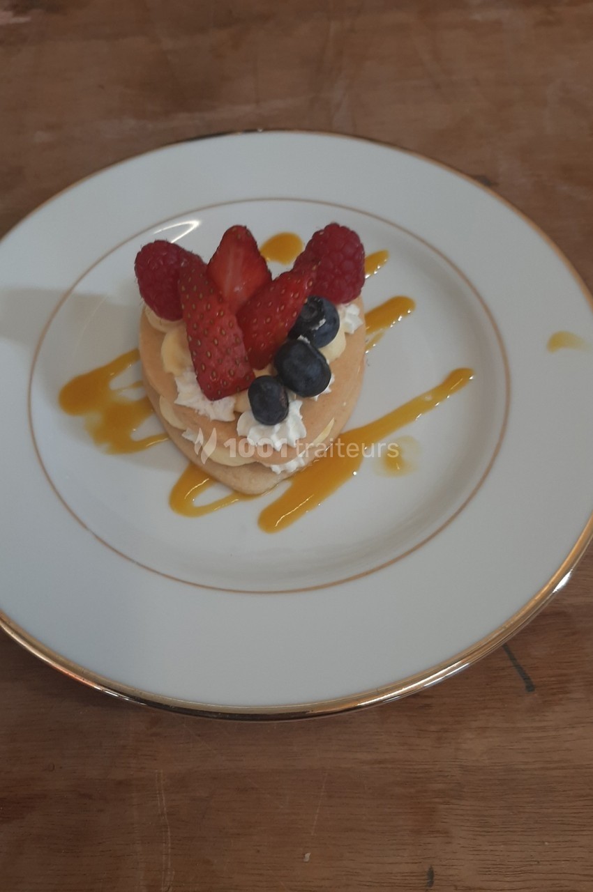 Assiette contenant un dessert composé de pancakes garnis de crème, fraises, framboises, myrtilles et coulis de mangue.