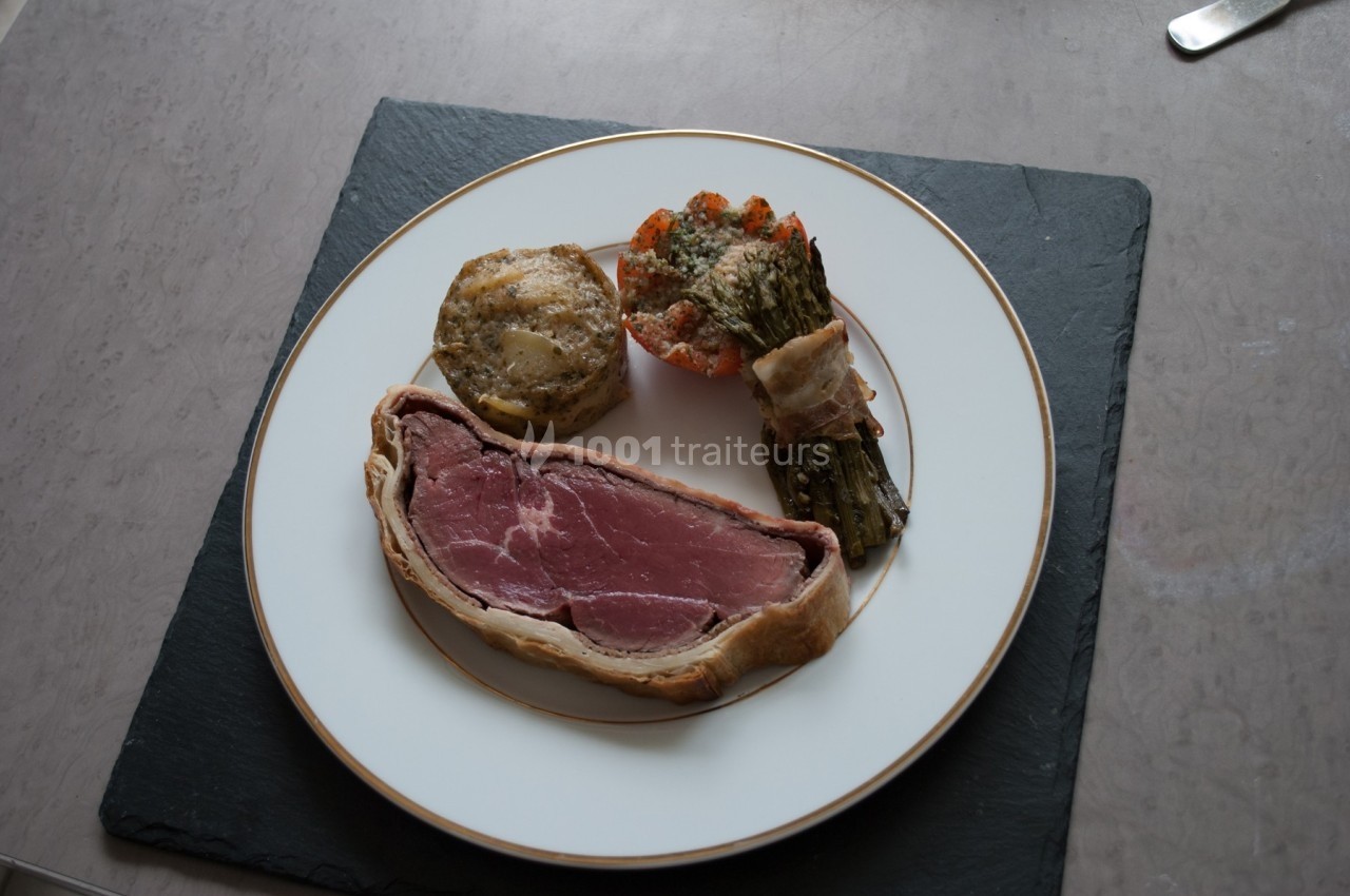 Assiette contenant un filet de viande en croûte, un gratin de pommes de terre, des légumes et une tomate garnie.