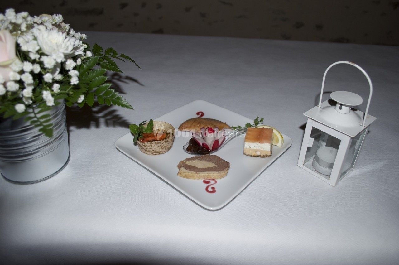 Assiette de canapés variés présentée sur une nappe blanche, avec une lanterne et un bouquet de fleurs en arrière-plan.