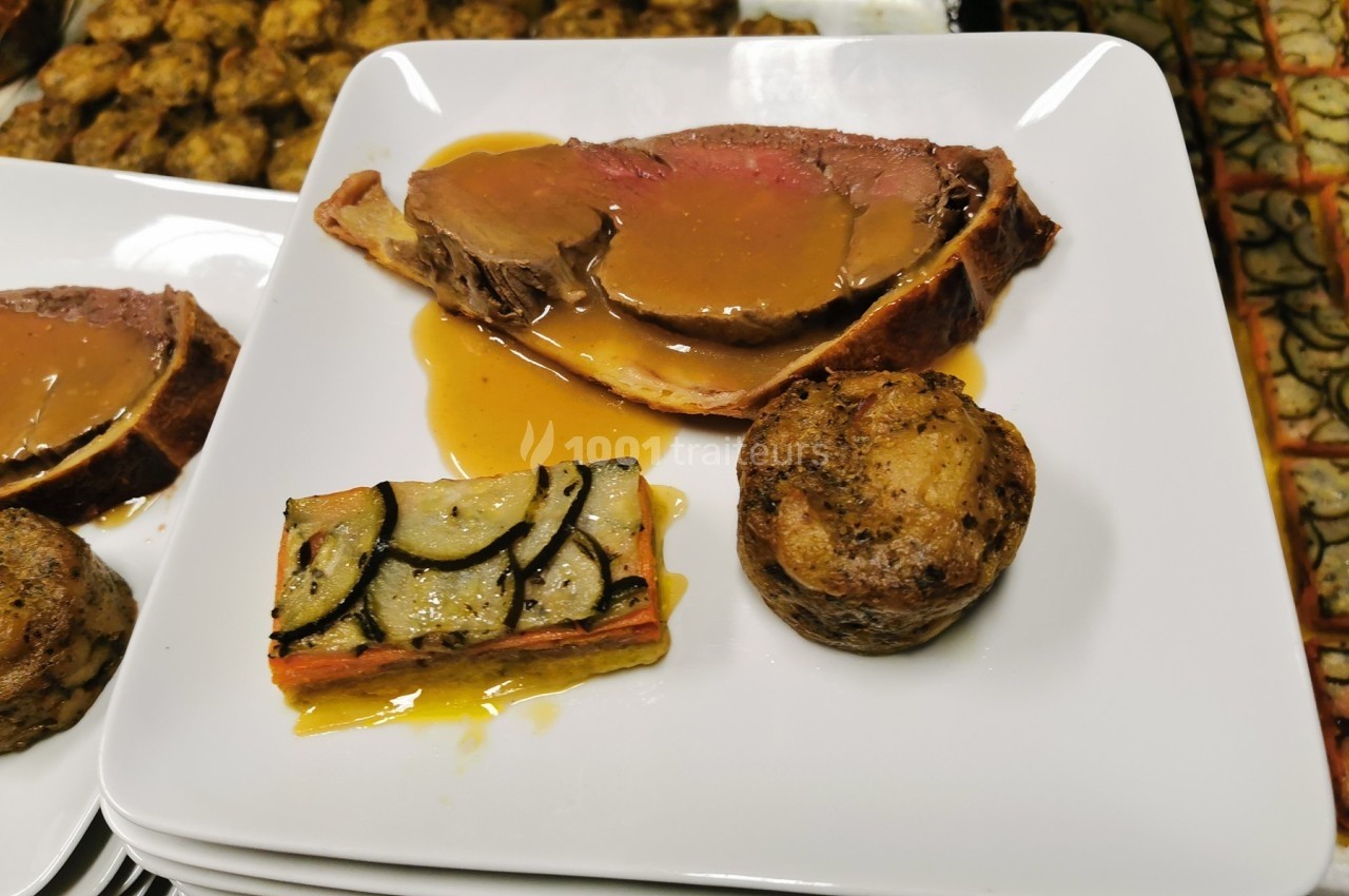 Assiette avec une tranche de viande en croûte et sauce, un gratin de légumes et une pomme de terre rôtie.