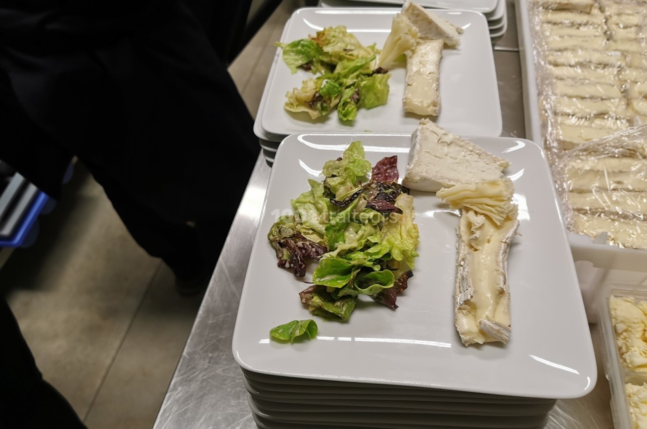 Assiette contenant une portion de salade verte et des morceaux de fromage, disposée sur un plan de travail.