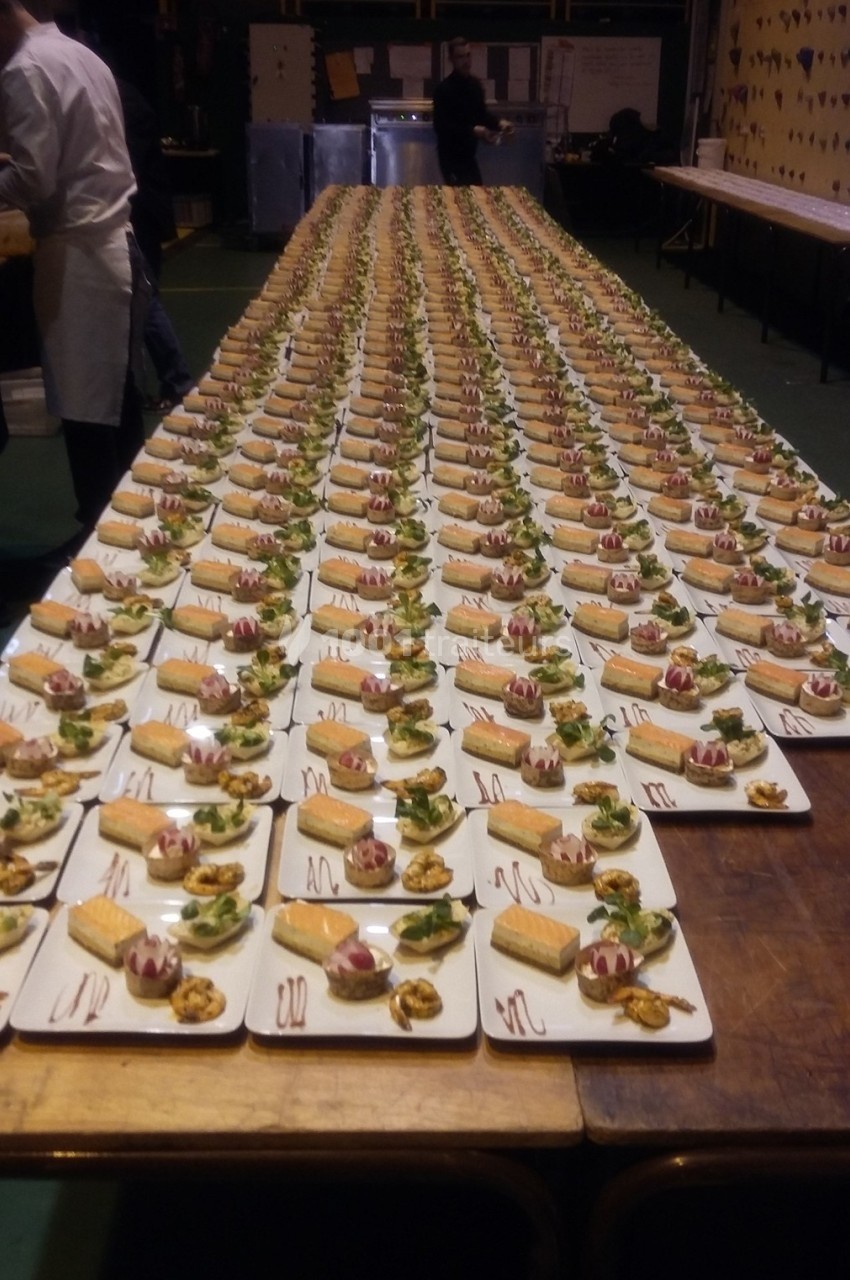 Des dizaines d'assiettes identiques alignées sur une longue table, contenant des desserts et des garnitures.
