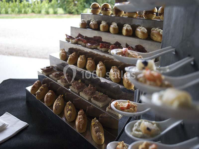 Présentoir avec des bouchées variées sur plusieurs étages et des cuillères garnies disposées sur le côté.