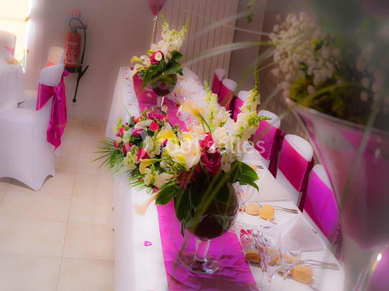 Salle décorée pour un événement avec une table ornée de fleurs colorées et nappes roses.