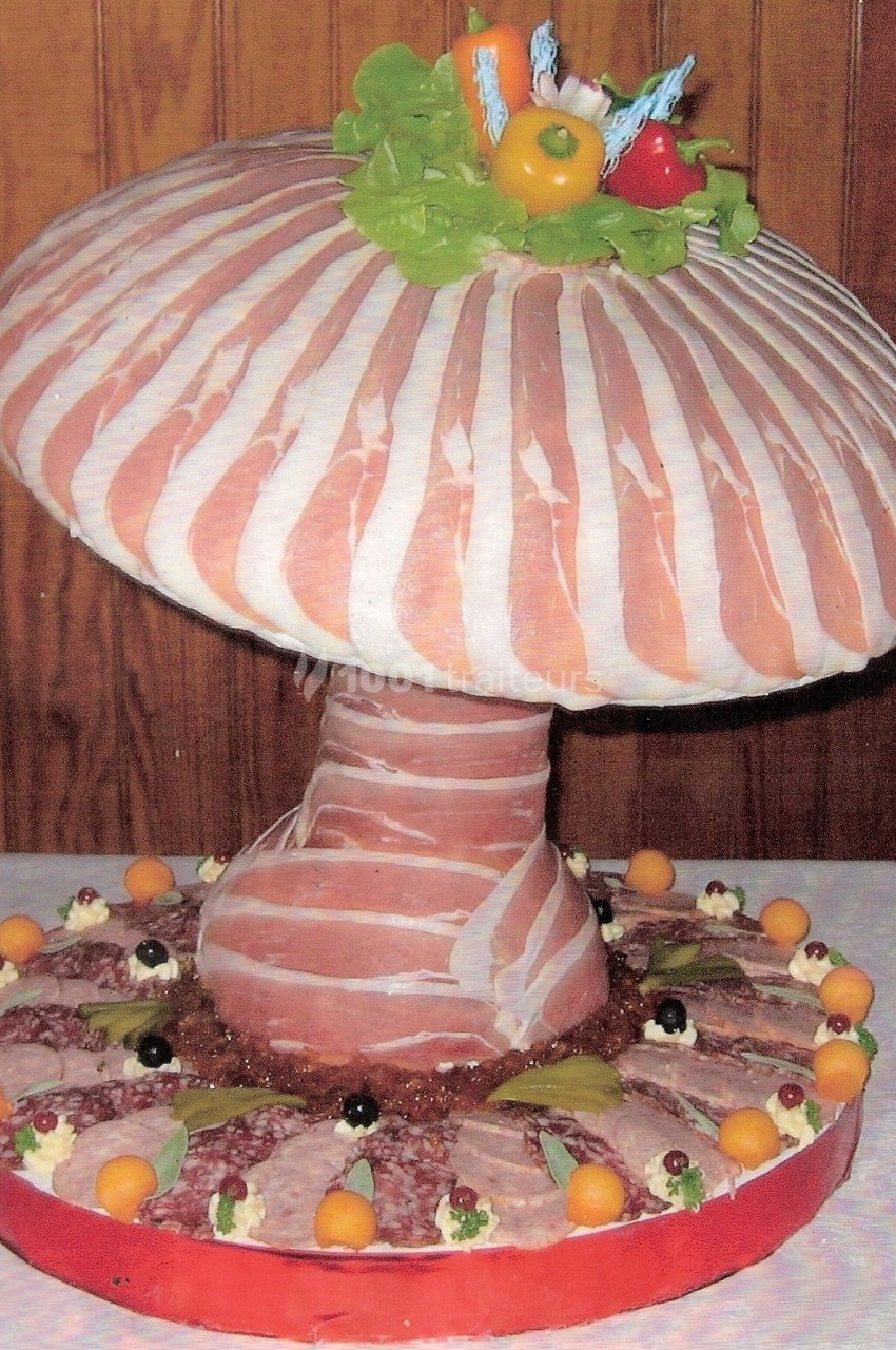 Plateau de charcuterie en forme de champignon, décoré de tranches de jambon, légumes et garnitures variées.