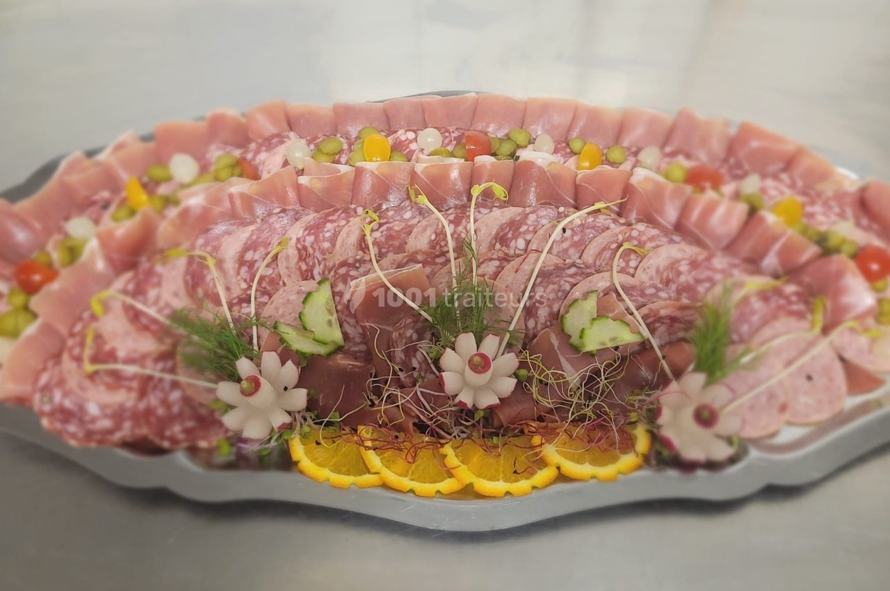 Plateau de charcuterie variée avec jambon, salami, légumes décoratifs et tranches d'agrumes sur un plat argenté.