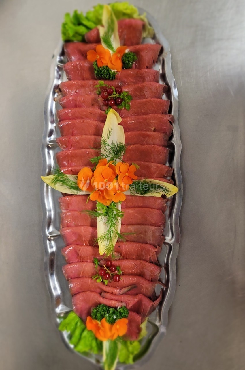Plateau de carpaccio de bœuf décoré de légumes, herbes fraîches et baies rouges sur un lit de salade.
