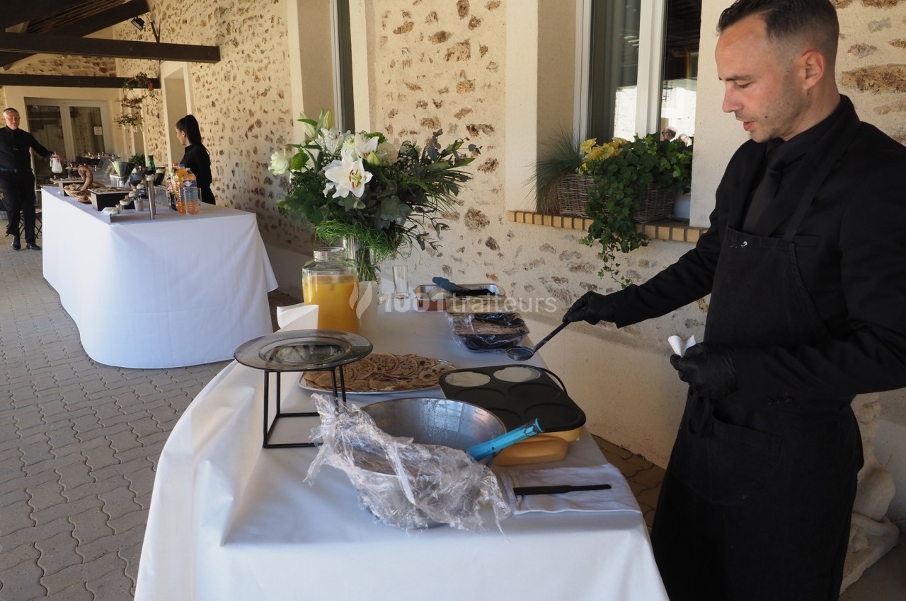 Un cuisinier prépare des crêpes sur une plaque chauffante lors d'un événement avec un buffet en arrière-plan.