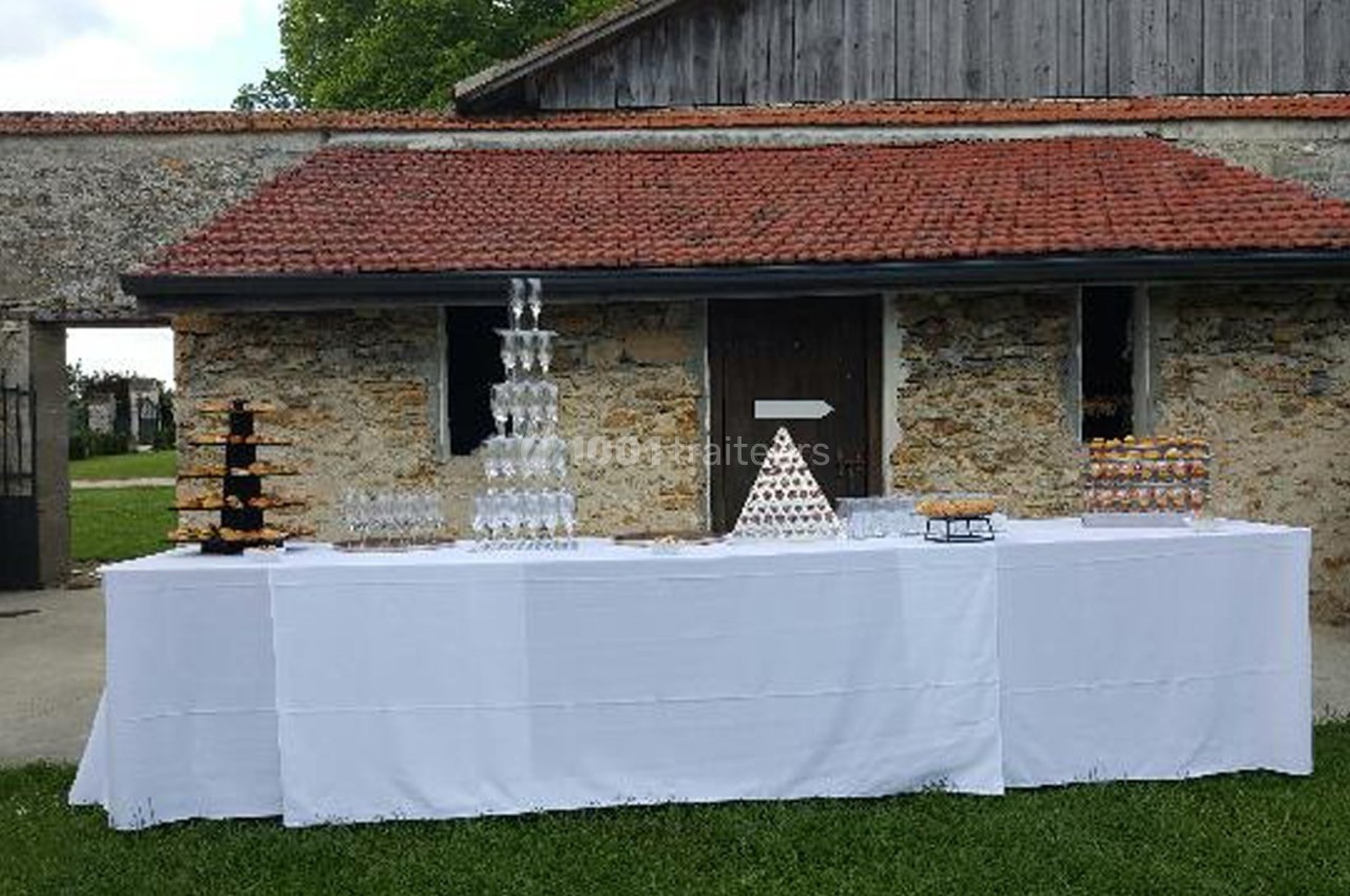 Table dressée en extérieur avec pyramides de coupes et de macarons devant un bâtiment en pierre et toit en tuiles.