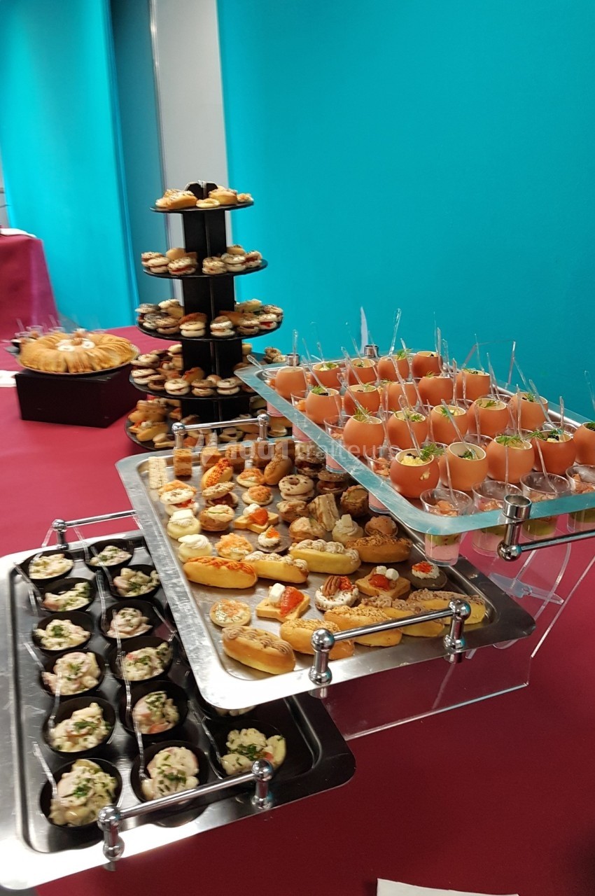 Buffet avec verrines, petits fours salés et sucrés disposés sur des plateaux et présentoirs devant un mur turquoise.