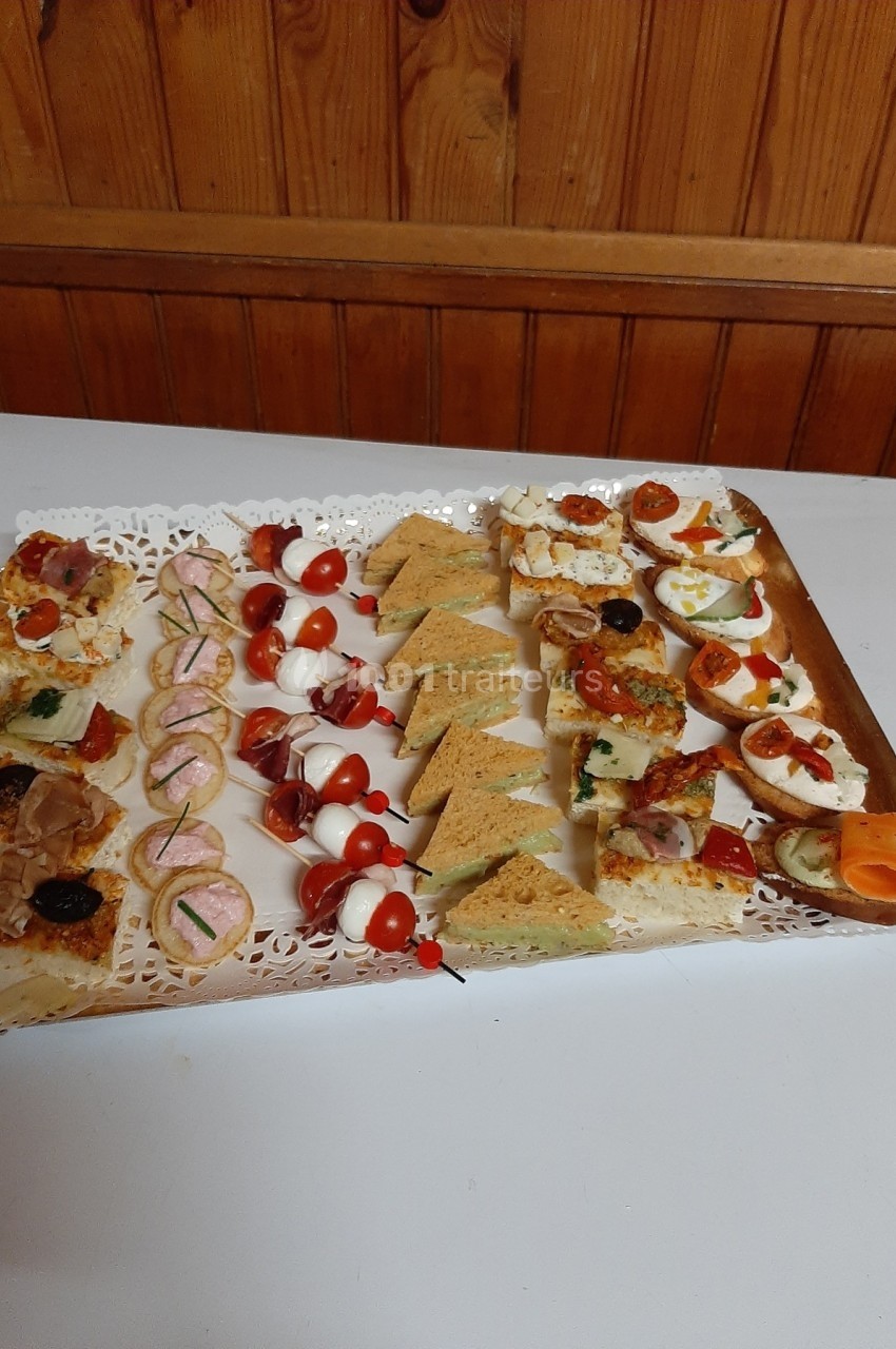 Plateau de canapés variés avec légumes, fromages, charcuteries et brochettes apéritives sur une table blanche.