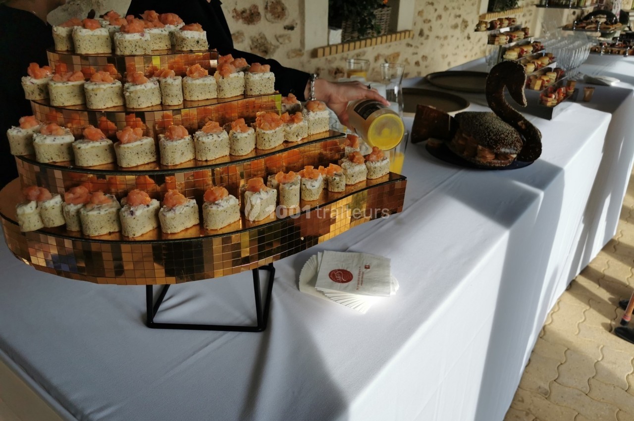 Présentoir doré avec verrines garnies de saumon, disposé sur une table blanche lors d'un buffet en extérieur.