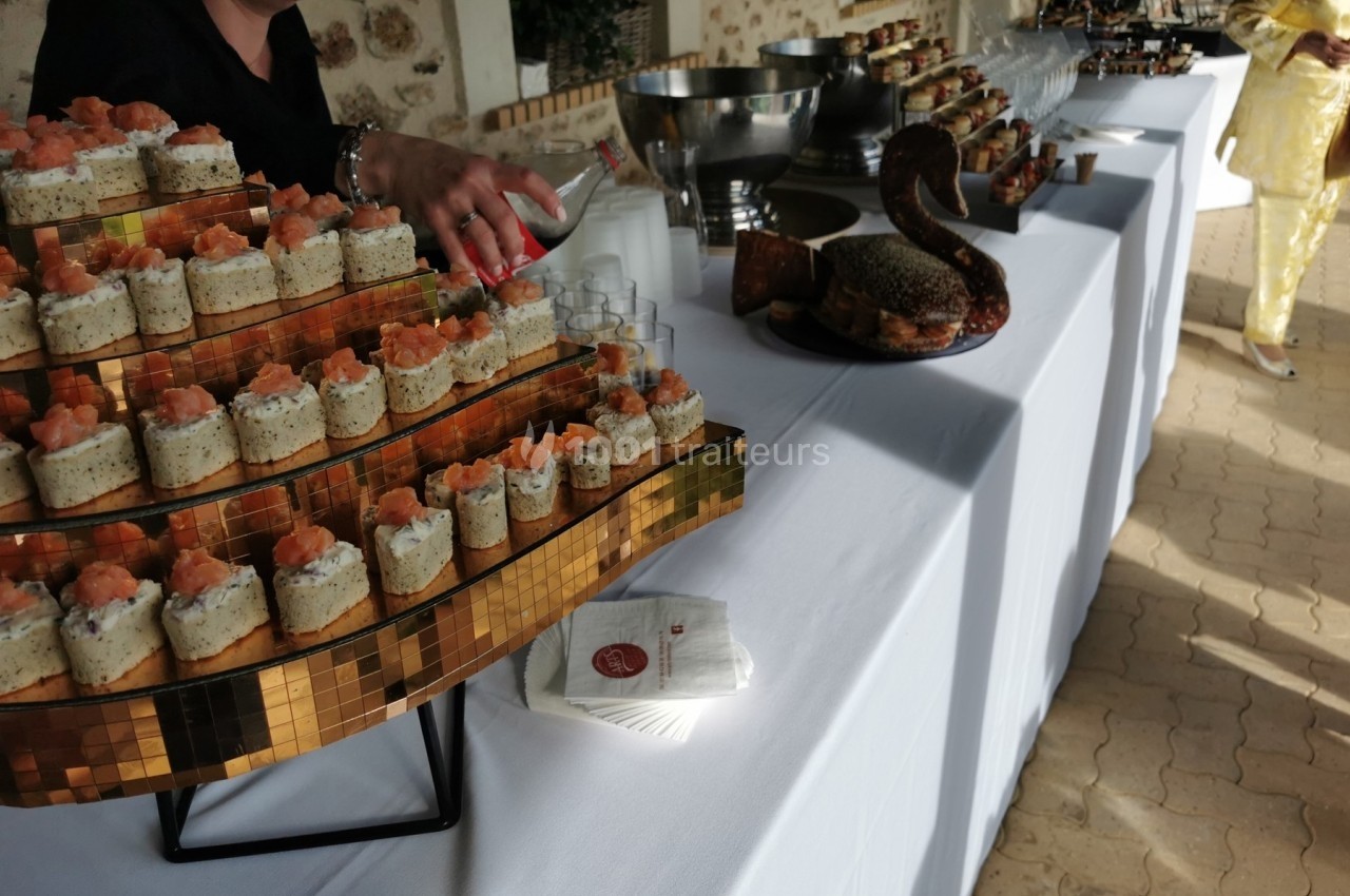 Plateau de toasts au saumon et buffet de réception dressés sur une table blanche en extérieur.