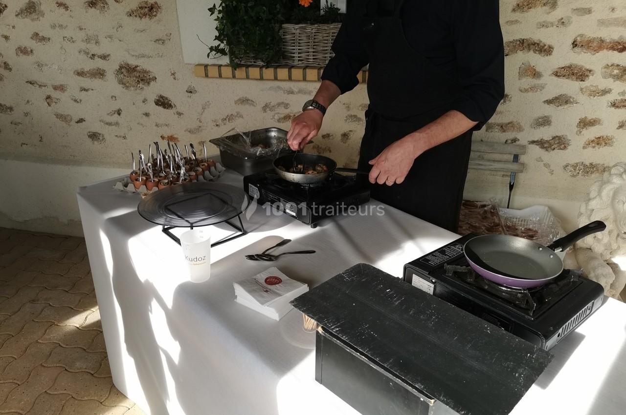 Un cuisinier prépare un plat chaud sur une table équipée de plaques de cuisson lors d'un événement en extérieur.