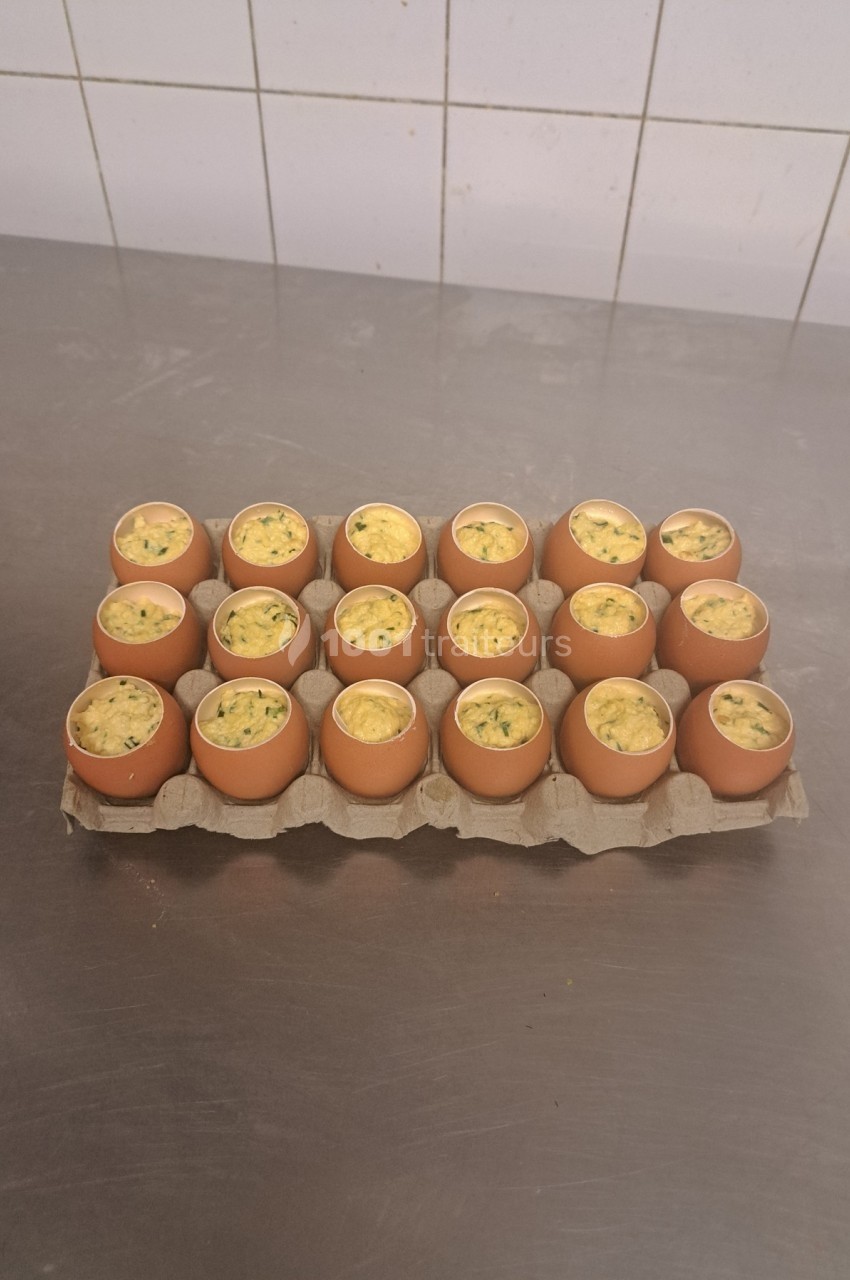 Plateau de coquilles d'œufs garnies d'une préparation cuisinée, disposé sur une table en inox.