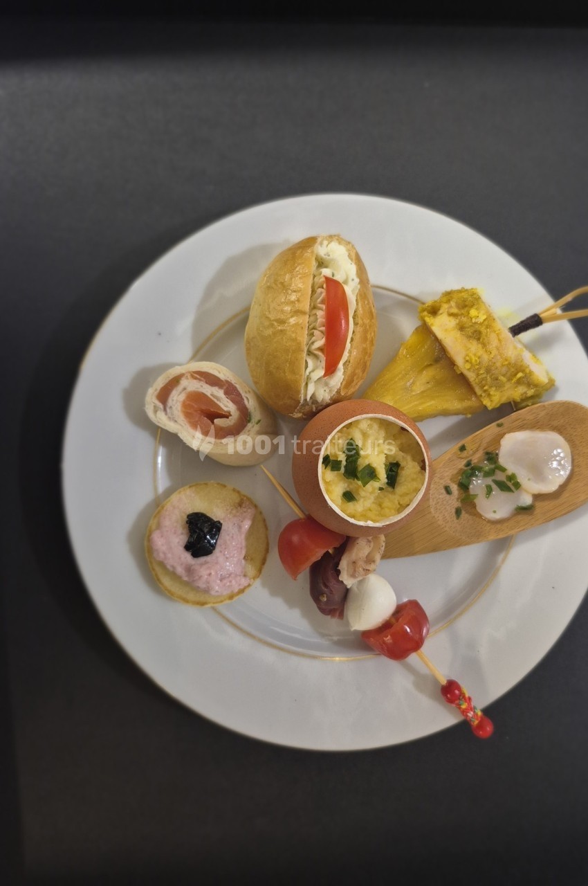 Assortiment de bouchées apéritives variées disposées sur une assiette blanche, présenté sur une table noire.