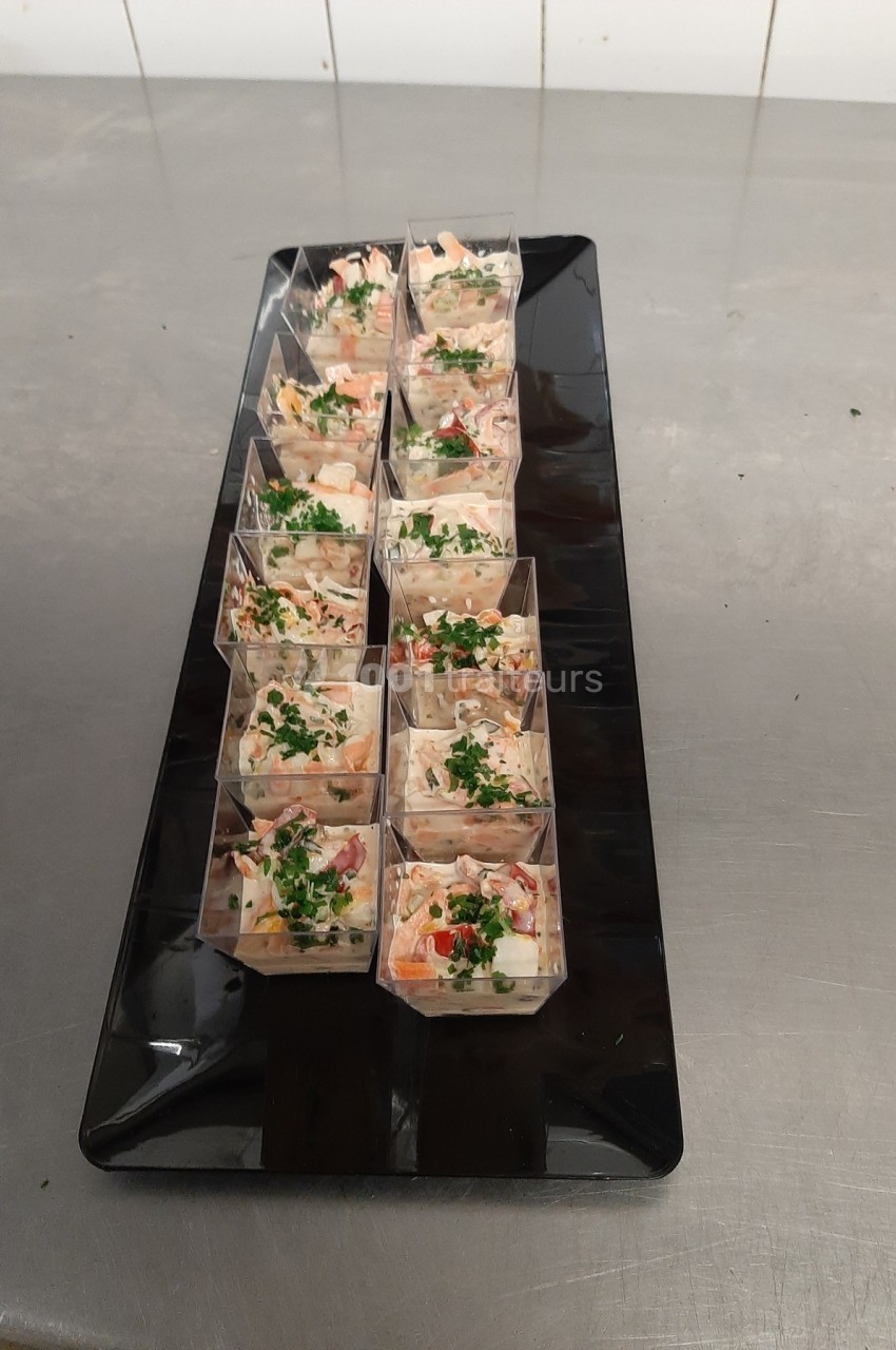 Plateau noir contenant des verrines garnies de salade colorée, décorées de persil frais, posé sur une table en inox.