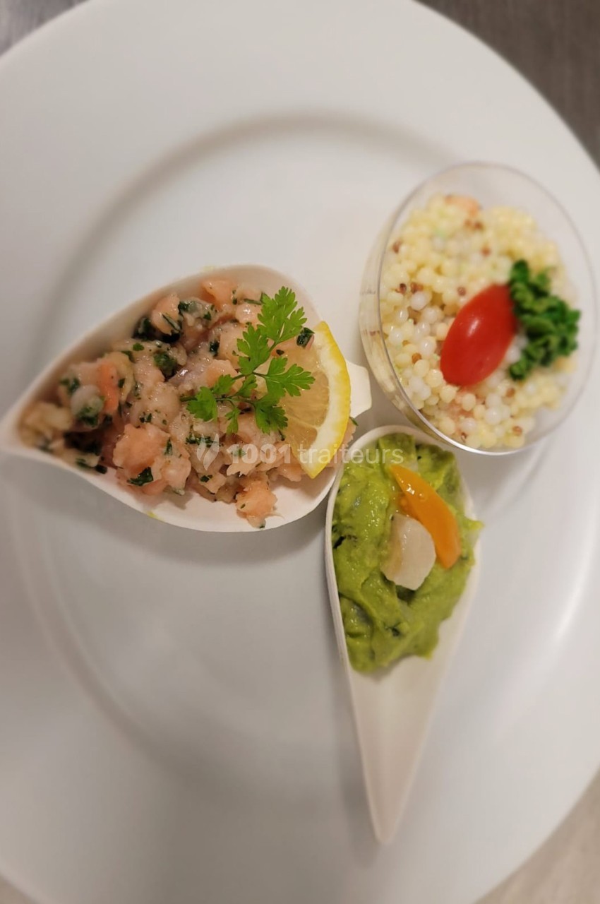 Assiette avec tartare de saumon, guacamole et perles de couscous garnies d'une tomate cerise et de persil.