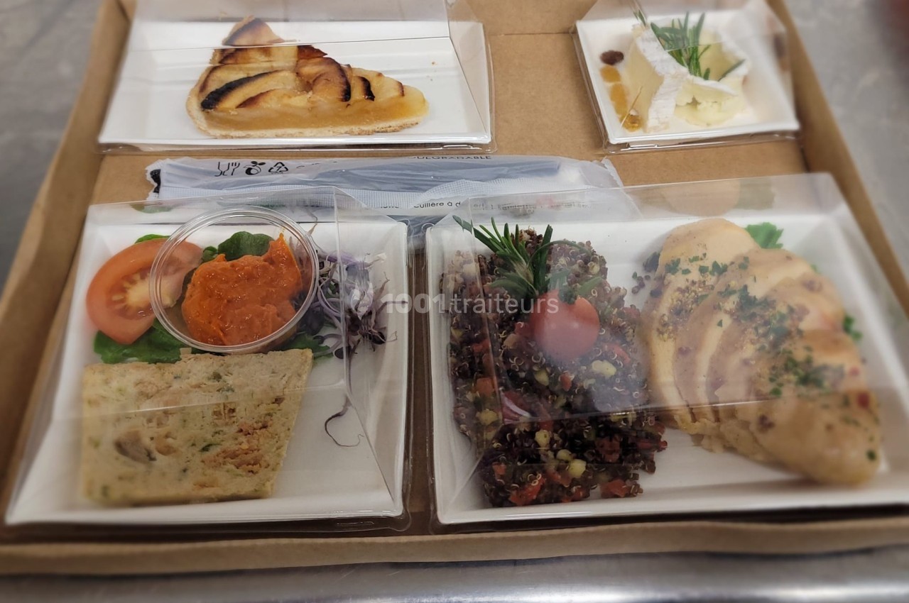 Plateau-repas avec poulet, quinoa, pain, tartinade, salade, fromage et tarte aux pommes, sous emballages transparents.