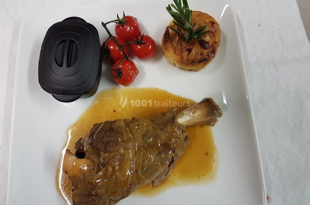 Assiette contenant un jarret d'agneau en sauce, des tomates cerises rôties, un gratin individuel et un couvercle noir.