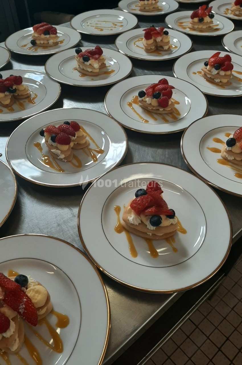 Assiettes de desserts individuels composés de fruits rouges, crème et caramel, alignées sur une table en cuisine.