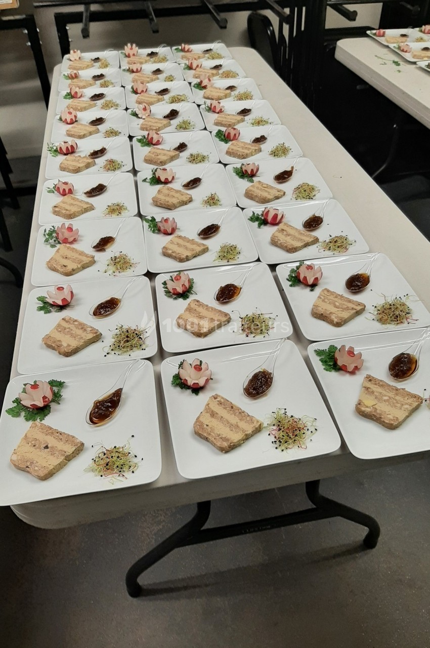 Assiettes dressées avec terrine, sauce, germes et décoration florale en cuisine collective.