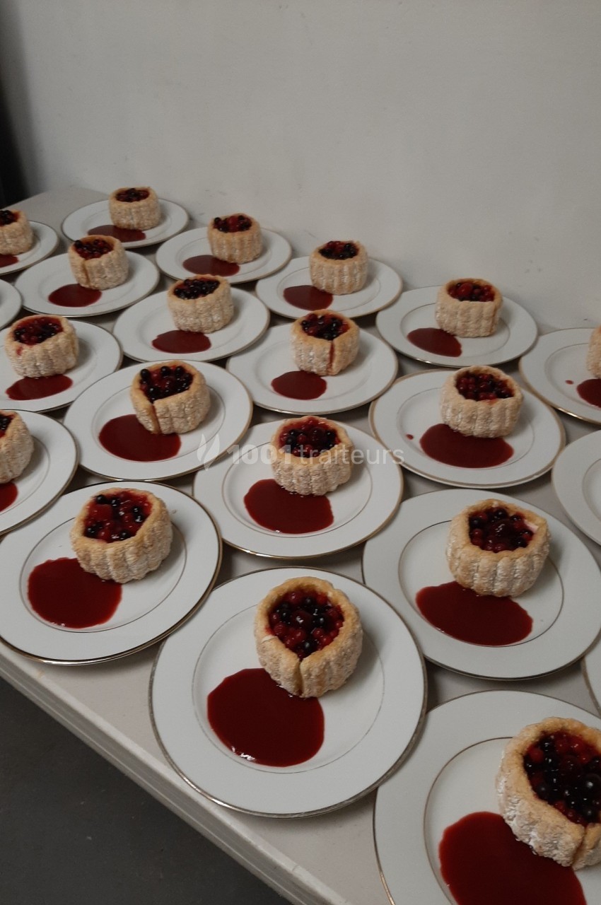 Assiettes alignées contenant des charlottes individuelles garnies de fruits rouges et entourées de coulis.