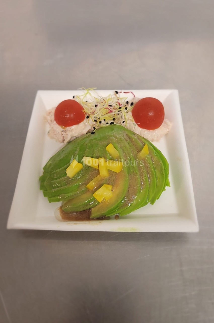 Assiette carrée contenant des tranches d'avocat, des tomates cerises, des germes et une garniture crémeuse.