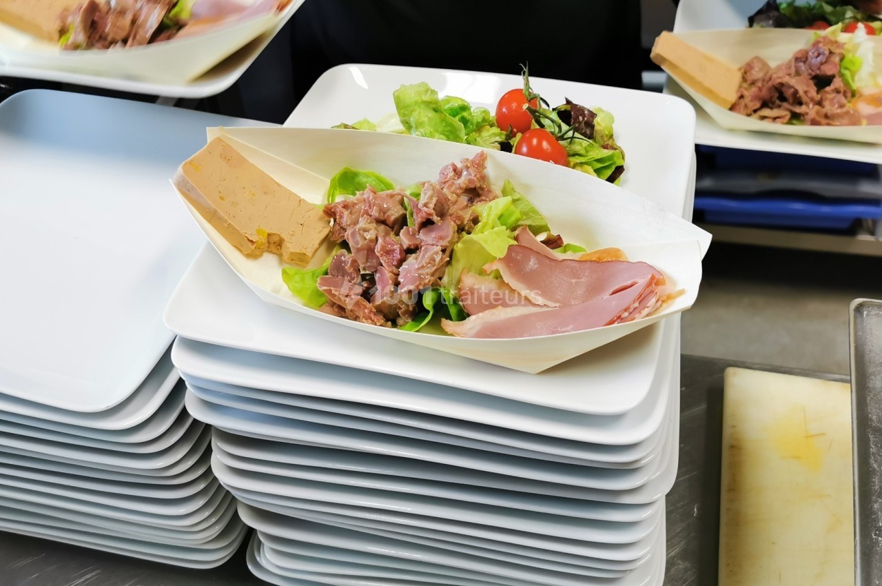 Assiette de charcuterie avec salade, tomates cerises et terrine, présentée sur un plateau empilé.