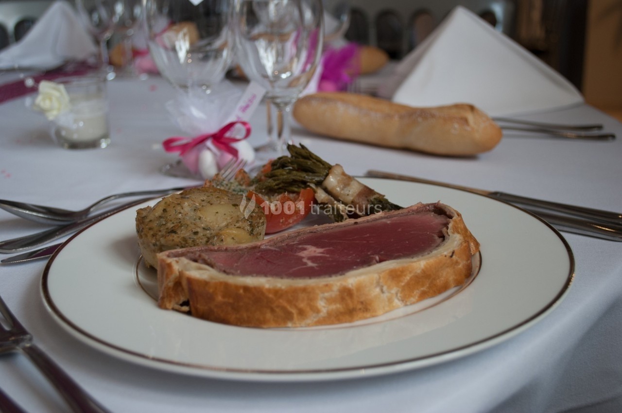 Assiette de bœuf en croûte accompagné d'asperges, tomate, pomme de terre et d'une baguette sur une table dressée.