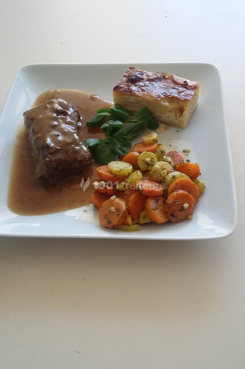 Assiette contenant un rôti en sauce, un gratin dauphinois et des légumes sautés colorés, servie sur une table blanche.
