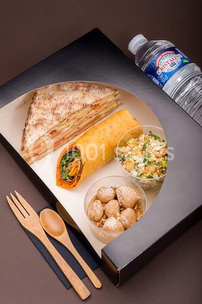 Plateau-repas composé d'un sandwich, d'un wrap, de taboulé, de pâtisseries, et d'une bouteille d'eau.