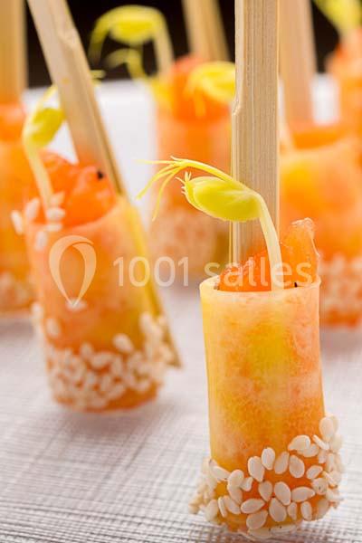 Bouchées apéritives roulées au saumon, garnies de graines de sésame et décorées de pousses vertes sur des piques.