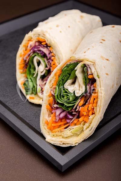 Deux wraps garnis de légumes frais, notamment carottes, chou rouge et feuilles de salade, présentés sur un plateau noir.