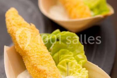 Dessert au chocolat brillant orné de feuille d'or, posé sur une base avec éclats de cacao, sur fond sombre.