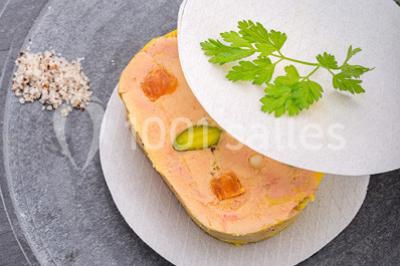 Dessert au chocolat brillant orné de feuille d'or, posé sur une base avec éclats de cacao, sur fond sombre.