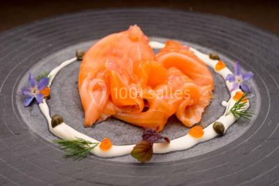 Dessert au chocolat brillant orné de feuille d'or, posé sur une base avec éclats de cacao, sur fond sombre.