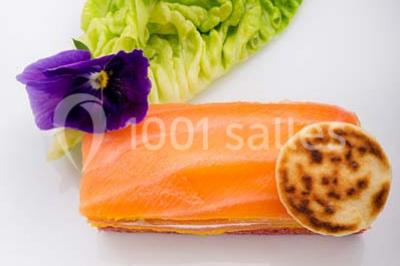 Dessert au chocolat brillant orné de feuille d'or, posé sur une base avec éclats de cacao, sur fond sombre.