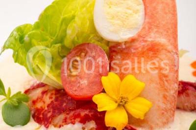 Dessert au chocolat brillant orné de feuille d'or, posé sur une base avec éclats de cacao, sur fond sombre.