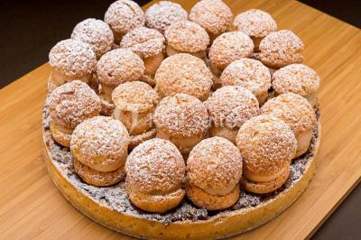 Dessert au chocolat brillant orné de feuille d'or, posé sur une base avec éclats de cacao, sur fond sombre.