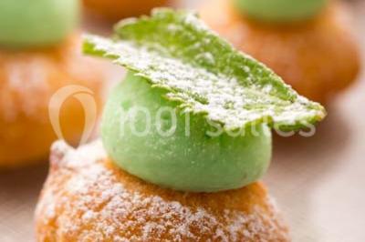 Dessert au chocolat brillant orné de feuille d'or, posé sur une base avec éclats de cacao, sur fond sombre.
