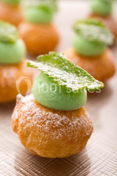 Chou pâtissier garni de crème verte, décoré d'une feuille saupoudrée de sucre glace, posé sur une surface dorée.