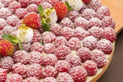 Dessert au chocolat brillant orné de feuille d'or, posé sur une base avec éclats de cacao, sur fond sombre.