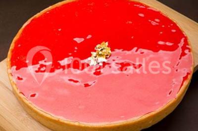 Dessert au chocolat brillant orné de feuille d'or, posé sur une base avec éclats de cacao, sur fond sombre.