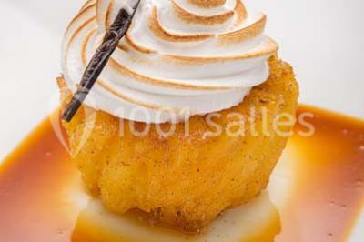 Dessert au chocolat brillant orné de feuille d'or, posé sur une base avec éclats de cacao, sur fond sombre.