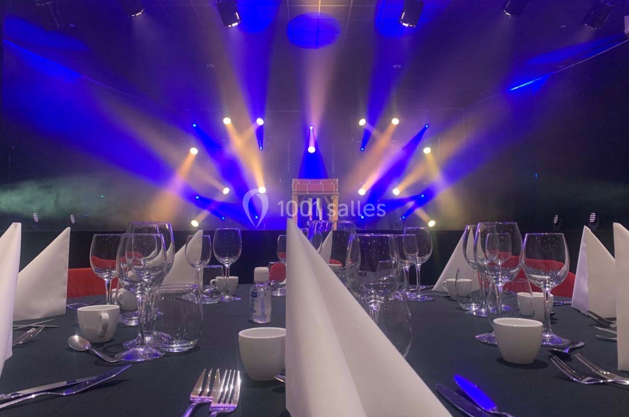 Salle de réception avec tables dressées et éclairage coloré sur une scène en arrière-plan.