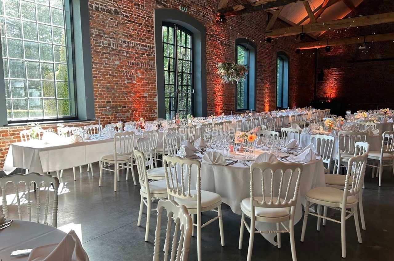 Salle de réception avec murs en briques, tables rondes dressées avec nappes blanches et chaises assorties.